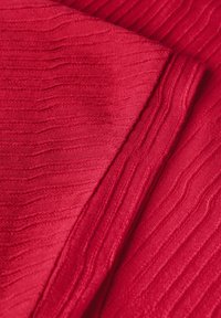 Tela texturizada roja con patrones de rayas horizontales, que muestra un tejido suave y apretado que crea una superficie táctil blanda.