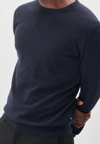 Lekki sweter w kolorze granatowym wykonany z miękkiego materiału, z okrągłym dekoltem, długimi rękawami i prążkowanym wykończeniem na dole. Posiada dyskretną metkę rozmiaru po bokach.