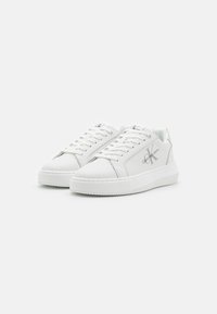 Sneaker bianche in pelle con suola in gomma testurizzata, chiusura con lacci e dettagli in argento che riportano il logo "Calvin Klein Jeans".
