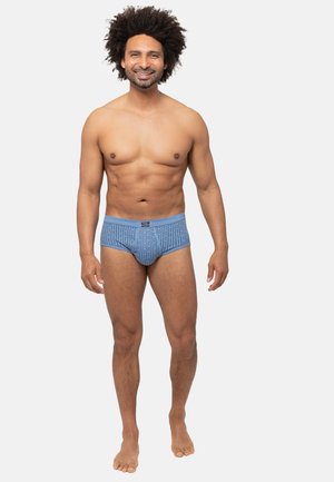 Blaue gemusterte Unterhosen mit elastischem Bund, mittelhohem Schnitt und enger Passform, präsentiert von einem männlichen Model vor einem neutralen Hintergrund.