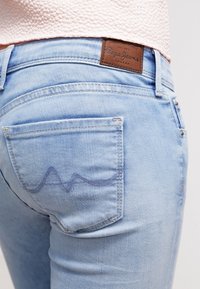Vaqueros de mezclilla de color azul claro con un bolsillo trasero que presenta un detalle de costura curva y una etiqueta de cuero con la marca en la cintura.