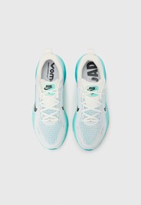 Scarpe da corsa bianche e azzurro chiaro con tomaia in mesh, lacci sottili e collo imbottito. Presentano un logo nero sul lato e suola turchese.