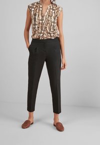 Bluzka z nadrukiem z dekoltem w kształcie V, krótki rękaw; czarne, dopasowane spodnie z kieszeniami po bokach; brązowe, plecione buty wsuwane.