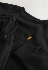 Schwarzer Sweatshirt und Jogginghose mit strukturiertem Stoff, gerippten Bündchen und einer kleinen gelben Hummerstickerei auf der Brust.