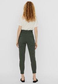 Pantalones de tiro alto en verde oliva, ajustados y con un corte entallado, que cuentan con bolsillos traseros y una textura suave. Se llevan con una blusa de color claro.