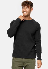 Mørkegrå langærmet sweater med ribbet tekstur, rund halsudskæring og raglanærmer, båret afslappet over grønne bukser.