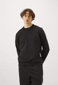 Sudadera negra de cuello redondo con puños y dobladillo de canalé, hecha de un tejido suave. Presenta una pequeña etiqueta de la marca en el costado.