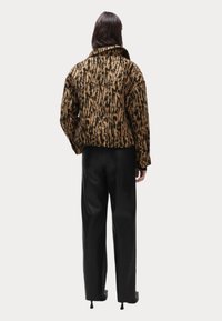 Veste en fausse fourrure avec un motif léopard dans des nuances de marron et de noir. Dispose d'un col, de manches longues et d'une silhouette ajustée.