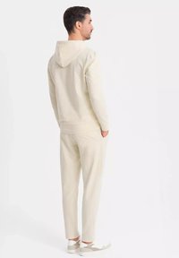 Cremefarbener Loungewear-Set bestehend aus einem Hoodie und taillierten Hosen. Weicher Stoff, gerippte Bündchen und Seitentaschen. Angenehme Passform und lässiges Design.
