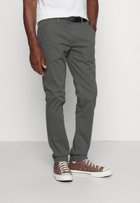 Szürke pamut chinos nadrág slim fit szabással, zsebekkel, barna vászon tornacipőkkel, fehér gumi talppal és fűzővel párosítva. Fekete öv kiemeli a megjelenést.