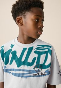 Weißes Baumwoll-T-Shirt mit kräftigem Türkis- und blauen Graffiti-Text und -Akzenten. Rundhalsausschnitt und kurze Ärmel, lässige Passform.