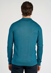 Teegrön stickad tröja med långa ärmar och ribbad krage, med en sömlös design och en figursydd silhuett.