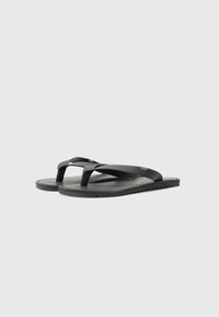 Svarte flip-flops med teksturerte gummistropper og en glatt såle. Fleksibel såle med taggete kanter for bedre grep. Enkel design uten dekorasjoner.