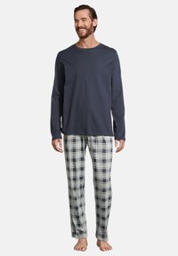 Mörkblå långärmad topp tillsammans med grå rutiga pyjamasbyxor, med mjuk textur, lös passform och elastisk midja. Barfota.