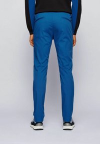 Blå byxor i lätt material, med smal passform, bakfickor och en slät yta. Matchas med svarta sneakers.