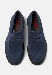 Blue suede slip-on shoes with a black sole, featuring a front strap and subtle cut-out design. Inside lining includes a red brand name.