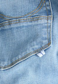 Nahaufnahme einer hellblauen Jeans-Tasche mit oranger Naht und einem kleinen weißen Stoffetikett mit blauen Punkten an der Seite.