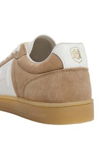 Suedesneakers och lädersneakers i beige och vitt, med en tan gummisula. Har en logotyp på hälen och kontrasterande sömmar.