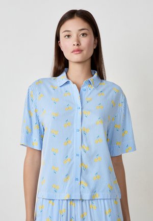 Chemise boutonnée en bleu clair avec des rayures blanches, dotée de motifs floraux jaunes. Manches courtes et design à col.