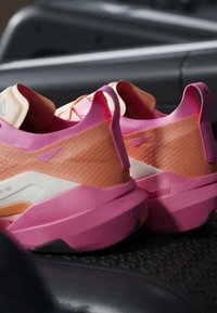 Paire de chaussures de sport roses et pêche avec des semelles épaisses placées sur une surface sombre texturée, montrant la vue arrière et latérale.