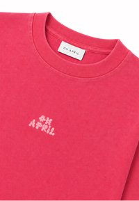 Hellrosa Crewneck-Shirt mit kleinem, hellrosa floralen "OH APRIL" Schriftzug auf der Brust und weißem "OH APRIL" Markenlabel im Kragen.