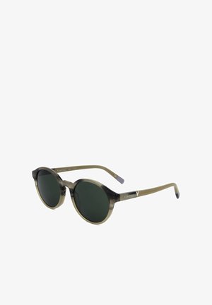 Occhiali da sole rotondi con lenti verde scuro e montatura e aste traslucide marrone-grigie, logo del marchio Vuarnet visibile sulle aste.