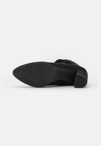 Talons en daim noir avec une semelle en caoutchouc texturée. Présente un bout légèrement arrondi et un petit talon empilé. Design simple sans ornements.