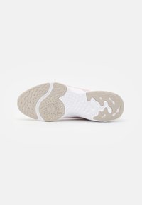 Suola di una sneakers rosa e bianca che mostra impugnature in gomma beige testurizzate e una suola intermedia bianca con motivi circolari in rilievo su sfondo bianco.