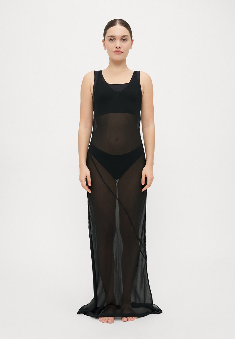 Fekete, áttetsző maxi ruha puha anyagból, ujjatlan kialakítással és testhezálló felső résszel, amely egy laza, lebegő szoknyába torkollik.