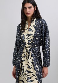 Togas largas con un estampado animal en negro y crema, con una cintura ceñida y mangas recogidas, fabricada en un tejido satinado.