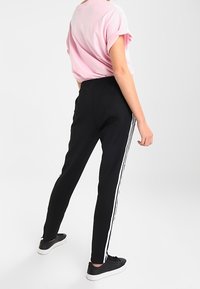 Black jogger pants with white side stripes, paired with a loose pink t-shirt. The fabric appears smooth, and shoes are black with a white sole.