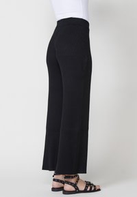Pantalons en tricot côtelé noir avec une taille haute ajustée, des jambes larges et des fentes en bas. Associés à des sandales noires à lanières.