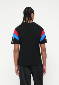 Tricou negru cu mânecă scurtă, având accente în dungi roșii, albastre și albe pe mâneci. Fabricat din bumbac, cu un croi lejer și o textură netedă.