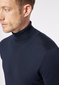 Navyblauer Rollkragenpullover aus einem weichen, gestrickten Stoff; taillierte Passform mit einem gerippten Kragen und glatter Textur, die eine elegante Silhouette betont.