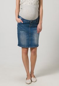 Džínová těhotenská sukně ve středně modré barvě, s klasickým pětikapsovým designem, rovného střihu a jemným vyblednutím. V kombinaci se šedým topem.