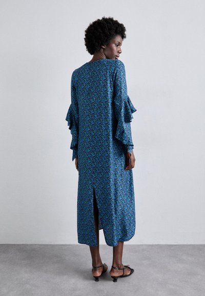 Blumenkleid in Blau mit Rüschensleeves, mittellang bis zur Wadenmitte und einem Schlitz hinten. Der Stoff hat eine weiche Textur mit einem sich wiederholenden Muster.
