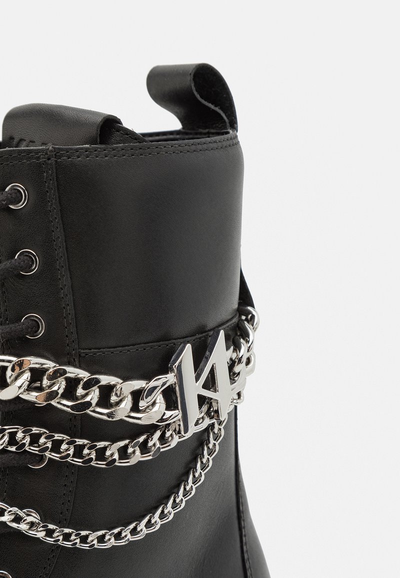 Schwarze Lederstiefel mit silbernen Kettenakzenten, Logo, Schnürdesign und einer Zuglasche oben. Glatte Textur und robuste Bauweise.