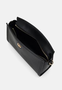 Černá kožená psaníčko s texturovaným povrchem, zlatým zipem a logem. Otevřený vršek odhaluje prostorný interiér.