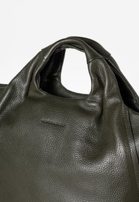 Borsa a tracolla in pelle verde scuro, con superficie testurizzata e un design morbido e sfilacciato, caratterizzato da impugnature arrotondate e ben in vista.