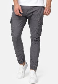 Graue Cargo-Hosen mit schmalem Schnitt, elastischem Bund, Reißverschluss-Bündchen und mehreren seitlichen Taschen. Kombination mit weißen Sneakers.