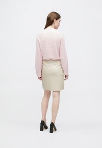 Růžový pletený svetr, béžová pouzdrová sukně a černé boty na blokovém podpatku. Oblečení má volný střih a hladkou texturu látky.