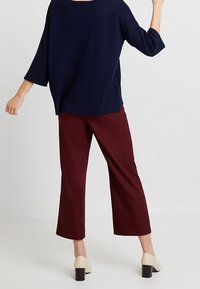 Granatowy, dziergany, oversize'owy top z rękawami do połowy ramienia, zestawiony z bordowymi, szerokimi spodniami i beżowymi butami na obcasie typu blok.