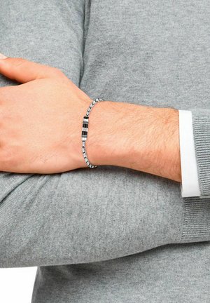 Bracciale in argento con catena, impreziosito da accenti neri rettangolari, con una finitura metallica liscia e link alternati, indossato su un polso.