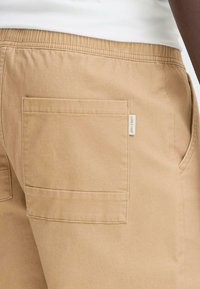 Khaki shorts laget av solid stoff, med elastisk midje og en baklomme med en liten etikett. Glatt tekstur og funksjonelt design.