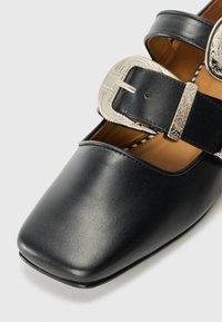 Black leather shoes with a square toe, featuring two decorative silver buckles on straps. Smooth texture and minimalistic design.