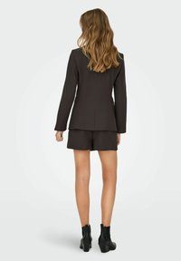 Ruda pritaikyta švarkas su ilgomis rankovėmis ir smailiais atlapais, derinamas su atitinkamais trumpais pantalonais, avimi juodais kulkšniais batais. Lygus audinys.