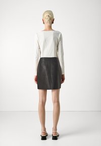 Bela dolga majica s long-sleeve rukavi, kombinirana s črnim usnjenim mini krilom, ki poudarja gladko teksturo in minimalističen dizajn.