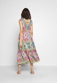 Abito maxi colorato con motivi floreali, colori vivaci, scollatura a V e dettaglio con lacci sul retro. Tessuto fluido e design a gonnellina a strati.