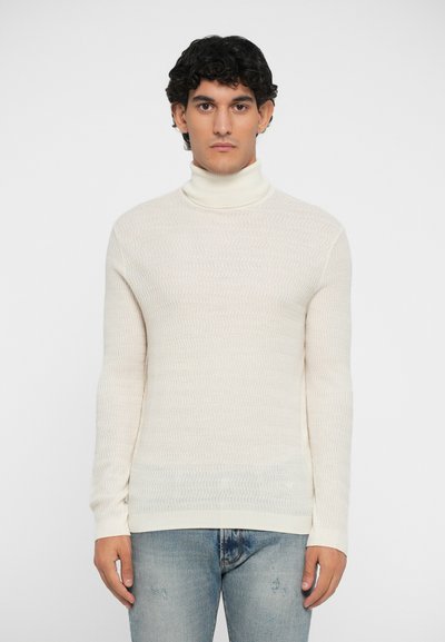 Cremfarbener Rollkragenpullover mit einem texturierten Wellenmuster. Enganliegendes Design mit gerippten Bündchen und Saum. Trägt man mit hellblauen, abgetragenen Jeans.