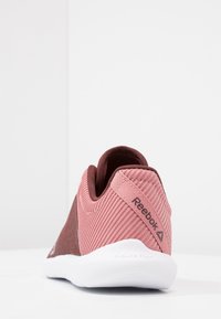 Reebok sportskor med en strukturerad överdel i rosa och brunt, rund häl och framträdande vit sula märkt "Sublite Foam."